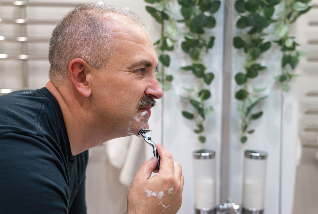 man scheert gezicht in badkamer